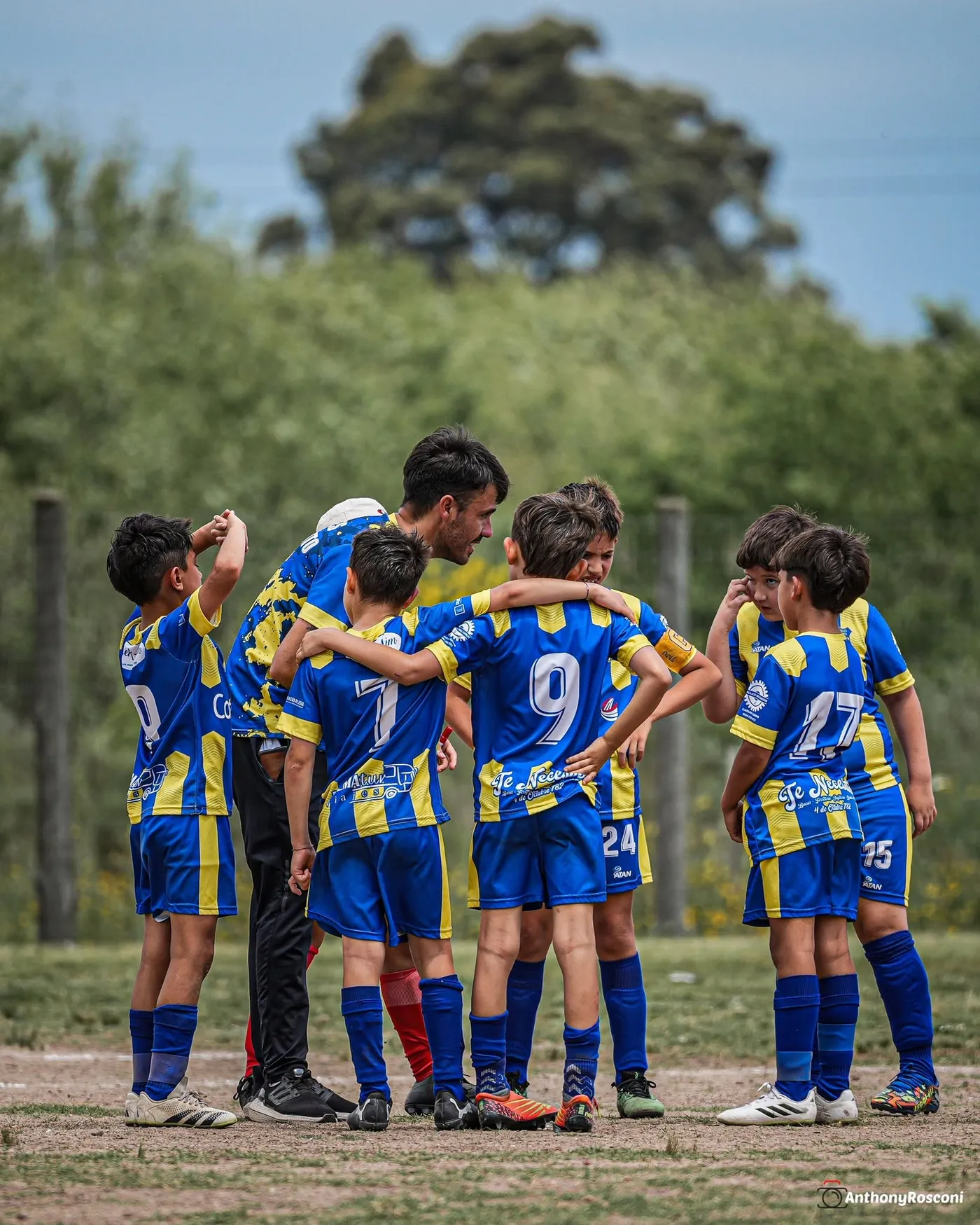 Un entrenador de Juveniles agachado, hablando con cinco jugadores en la cancha